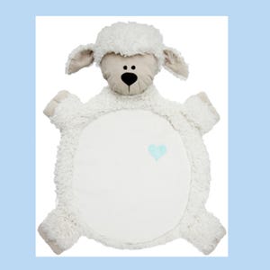 May include: A plush, white sheep-shaped baby blanket with a light blue heart applique. The sheep has a beige face, ears, and paws, and a fluffy, textured body. The blanket is designed for comfort and is likely for a baby.