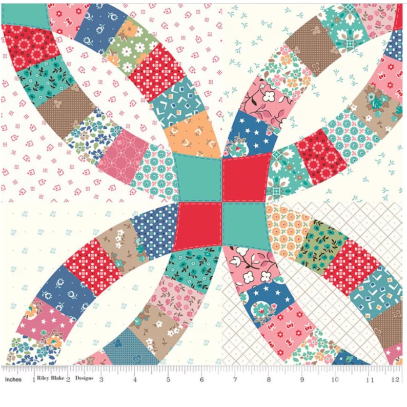 May include: A colorful patchwork fabric square featuring a double wedding ring design. The quilt block showcases a variety of floral and geometric patterns in shades of red, blue, pink, and teal, with a cream background. The fabric is marked with inches.