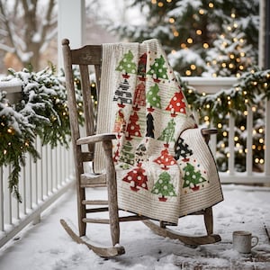 May include: A wooden rocking chair draped with a quilt featuring a repeating pattern of stylized Christmas trees in various shades of red, green, and black, set against a light-colored background with printed text details throughout the fabric.