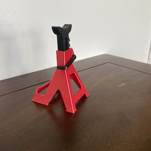 May include: A red and black plastic car jack stand. The stand is in the shape of a triangle with a black metal top.