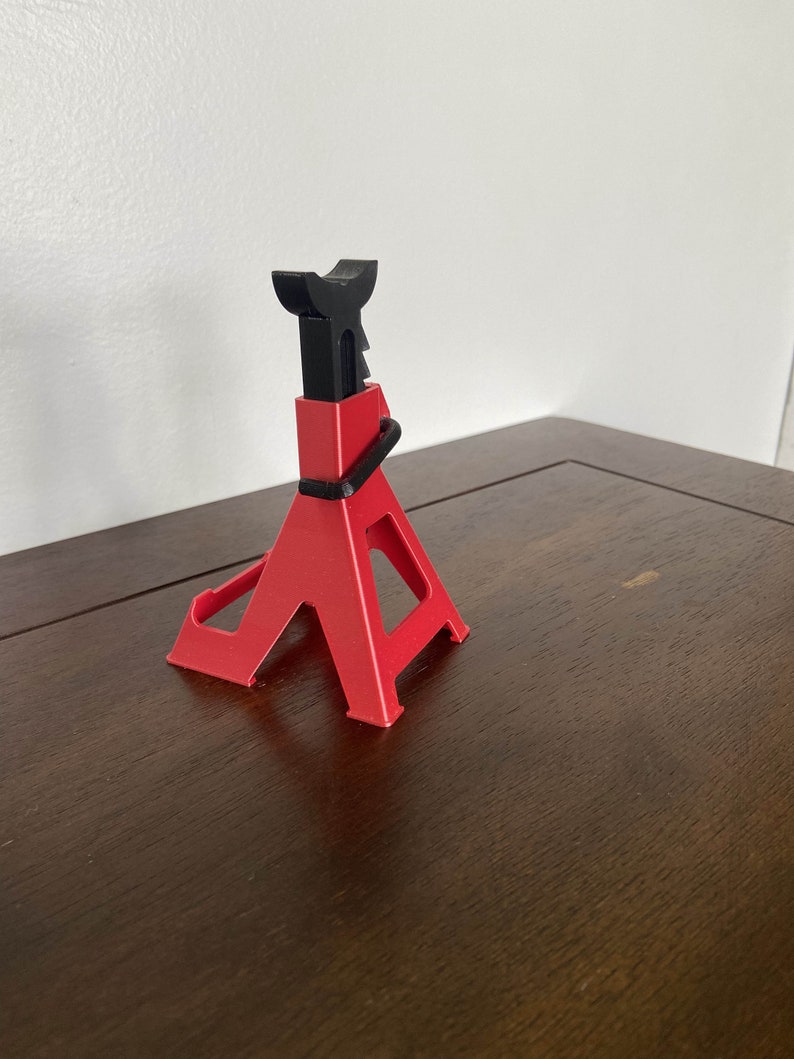 May include: A red and black plastic car jack stand. The stand is in the shape of a triangle with a black metal top.