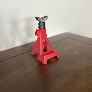 May include: A red and black plastic car jack stand, a miniature version of a real car jack stand, used as a phone stand.