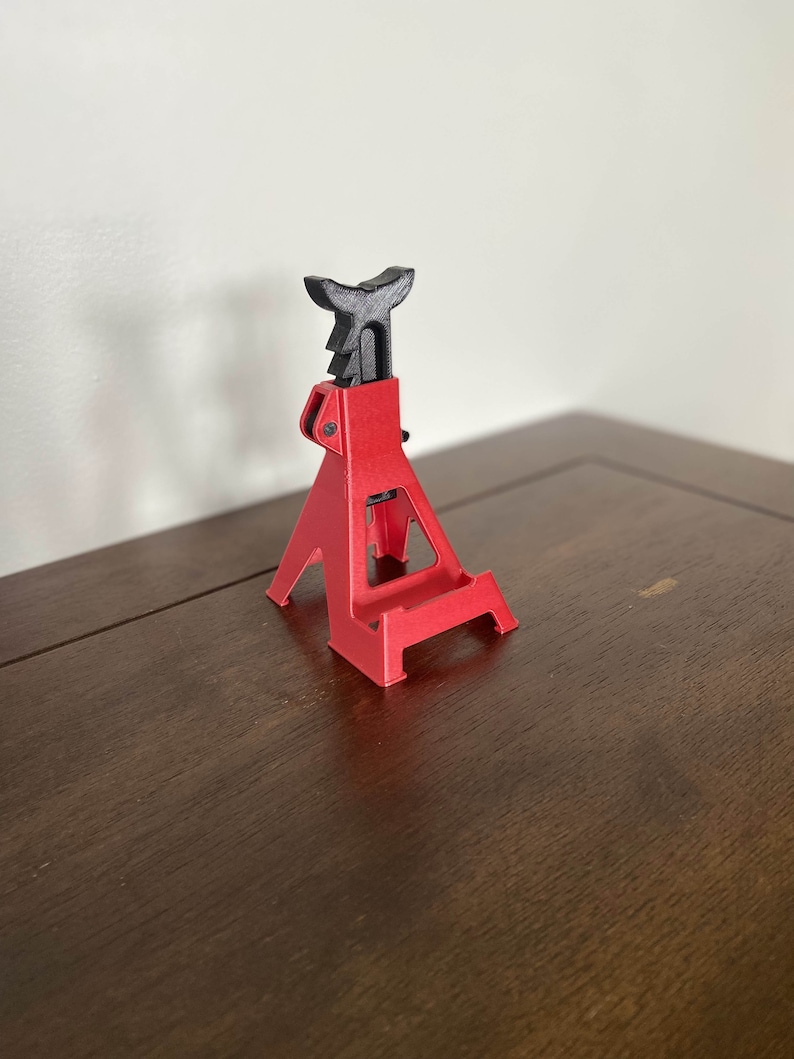 May include: A red and black plastic car jack stand, a miniature version of a real car jack stand, used as a phone stand.