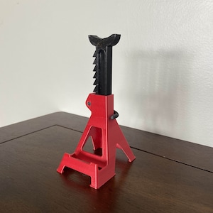 May include: A red and black plastic car jack stand. The stand is designed to hold a car up while it is being worked on.