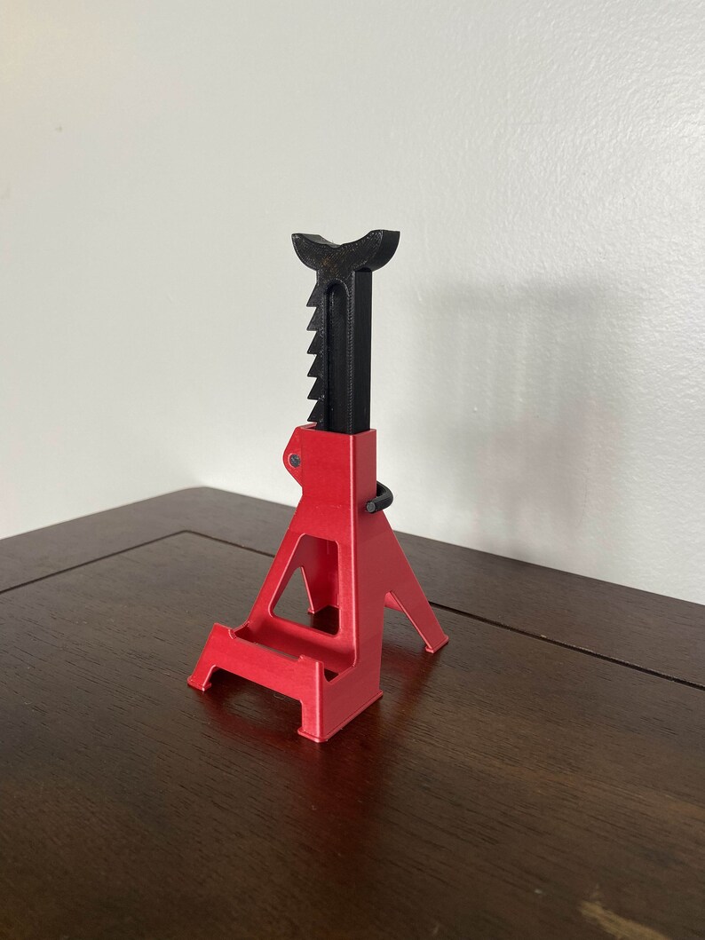 May include: A red and black plastic car jack stand. The stand is designed to hold a car up while it is being worked on.