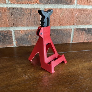 May include: A red plastic phone stand shaped like a car jack. The stand has a black plastic handle and a textured surface.
