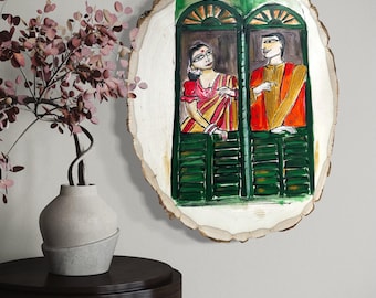 May include: A hand-painted artwork on a wood slice depicts two figures in a window. The figures are dressed in traditional attire, with the woman in a red and yellow sari. The window has green shutters.