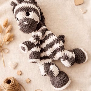 May include: A crocheted zebra stuffed animal featuring alternating horizontal stripes of dark gray and white yarn. The plush toy has a rounded head with dark eyes, a short mane, four limbs, and a small tail, all crafted with a soft, textured stitch.