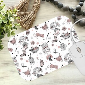 May include: White mouse pad with a repeating pattern of girls knitting, yarn balls, needles, and hearts. The pattern is in black and pink.