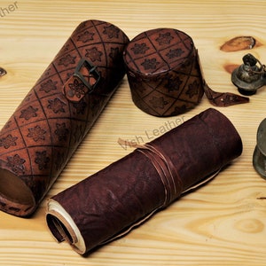 Könnte beinhalten: Ein Set aus Leder-Schreibutensilien, bestehend aus einem aufgerollten Journal, einem Füllhalter und einem kleinen Tintenfass. Das Leder ist braun und hat ein dekoratives Muster.