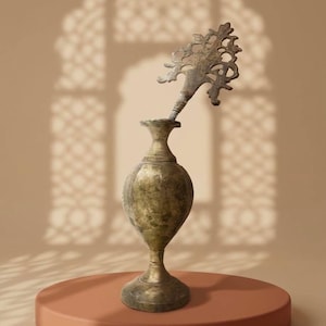 May include: An antique brass vase with a decorative tree-like applicator. The vase has a bulbous body and a slender base, standing on a round, terracotta-coloured platform. The background features a soft, neutral colour palette with a patterned shadow.