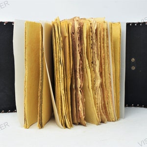 May include: A brown leather-bound journal with a clasp closure. The journal has a rustic look and is open to reveal pages of handmade paper.