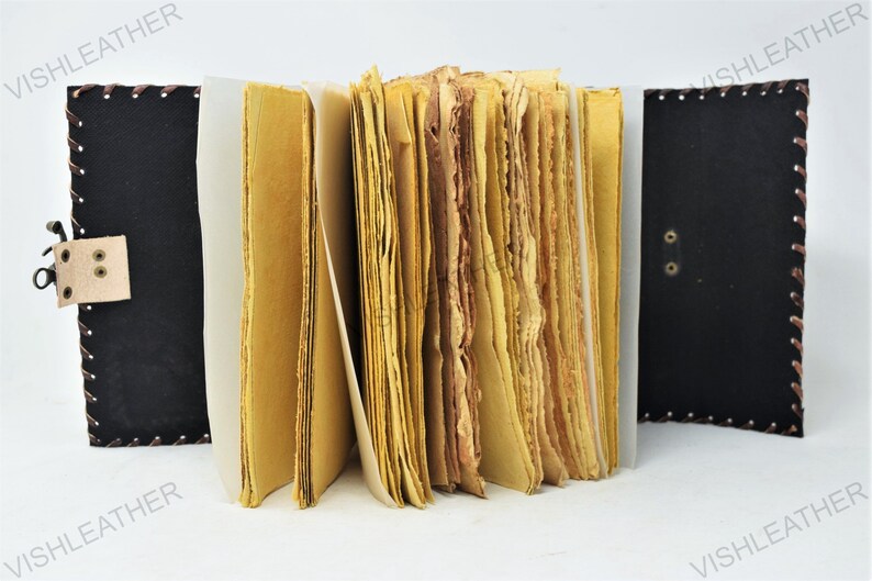 May include: A brown leather-bound journal with a clasp closure. The journal has a rustic look and is open to reveal pages of handmade paper.
