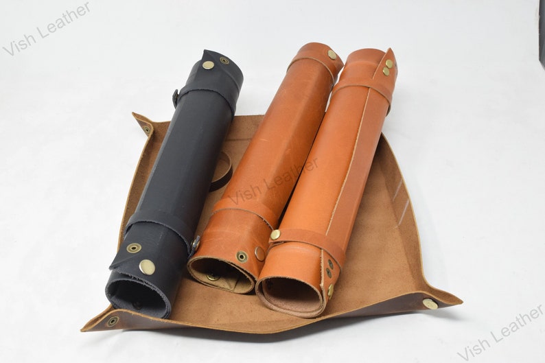 May include: Three leather rolls, one black and two brown, are displayed in a brown leather tray. The rolls have brass buckles and snaps.
