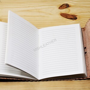 May include: A brown leather-bound journal with lined pages is open on a wooden surface. The journal has a decorative stitching detail on the cover.