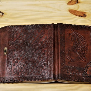 May include: A brown leather journal with a dragon design embossed on the front cover. The journal has a decorative clasp and a gemstone accent.