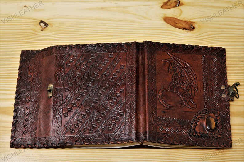 May include: A brown leather journal with a dragon design embossed on the front cover. The journal has a decorative clasp and a gemstone accent.