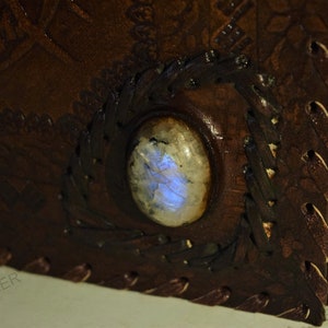 May include: A brown leather journal with a decorative design and a blue iridescent gemstone set into the cover.