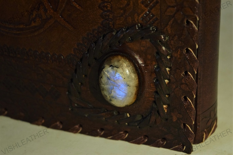 May include: A brown leather journal with a decorative design and a blue iridescent gemstone set into the cover.