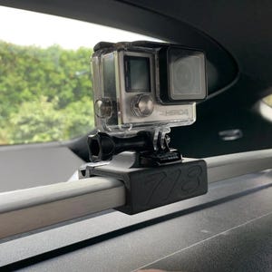 Puede incluir: Una cámara GoPro Hero4 negra montada en un soporte negro con el número 718 impreso en él. La cámara está unida a una barra de metal plateada.