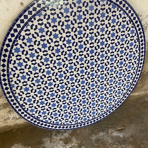 May include: A round table top with a blue and white geometric mosaic tile design. The tile pattern features a repeating star shape.