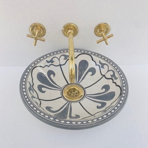 May include: A white ceramic sink with a blue and white floral design. The sink has a brass faucet with a single handle and two brass knobs.