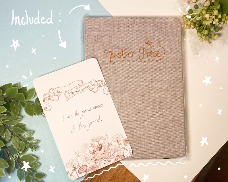 May include: A beige journal with the text "misster Press" in brown cursive lettering. The journal is accompanied by a card with a floral design and the text "Solemnly swear I am the proud owner of this journal."