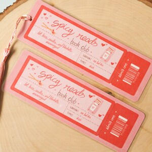 May include: Two pink and red bookmark tickets with the text "Spicy Reads Book Club" and "Admit One". The tickets have a graphic of a matchstick and a heart.