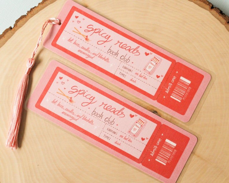 May include: Two pink and red bookmark tickets with the text "Spicy Reads Book Club" and "Admit One". The tickets have a graphic of a matchstick and a heart.
