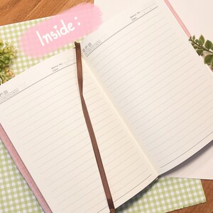 May include: An open pink notebook with lined pages and a brown ribbon bookmark. The notebook is lying open on a green and white checkered surface. The words "Inside:" are written in pink on a white background.