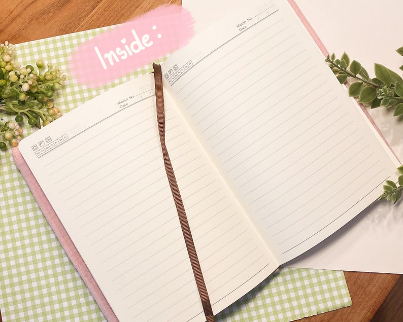 May include: An open pink notebook with lined pages and a brown ribbon bookmark. The notebook is lying open on a green and white checkered surface. The words "Inside:" are written in pink on a white background.