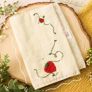 May include: A white fabric pouch with embroidered strawberries and vines. The pouch has a small tag that says "Made with Love".