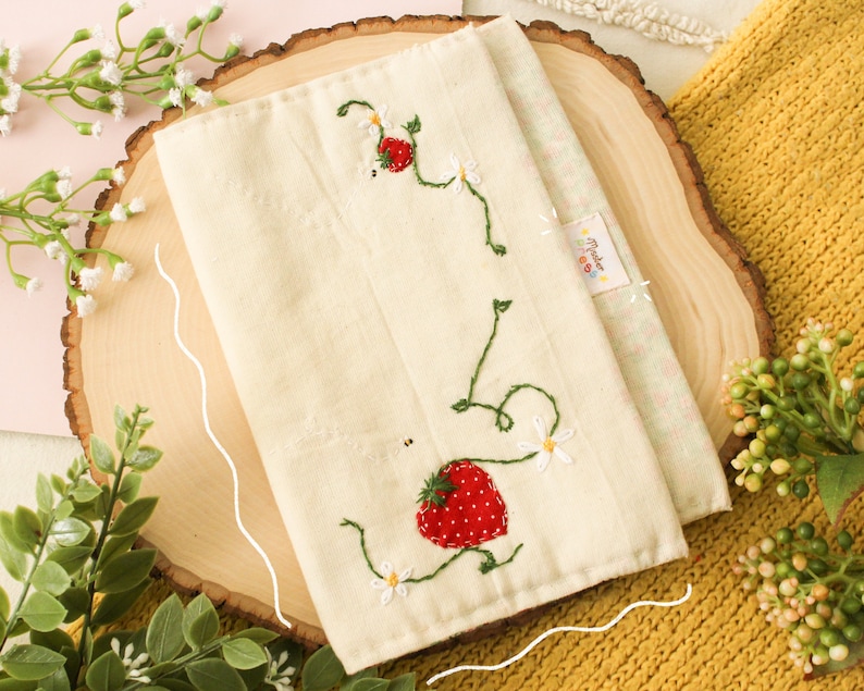 May include: A white fabric pouch with embroidered strawberries and vines. The pouch has a small tag that says "Made with Love".