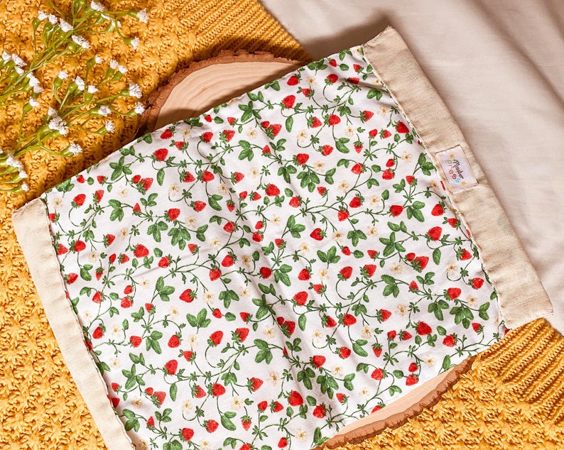 May include: A white fabric bag with a strawberry print and a beige fabric border. The bag has a small label with the text "Made with Love" on it.