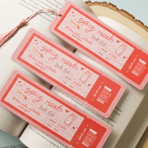 May include: Three pink bookmarks with a whimsical design featuring a book, matches, and the text "Spicy Reads Book Club". The bookmarks have a ticket-style design with the text "Admit One" and a barcode.