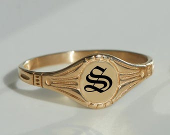 May include: A gold signet ring with a black letter "S" engraved in an old English font.