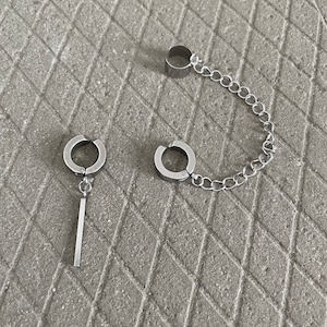 May include: Two silver hoop earrings with a connecting chain. One earring has a straight bar pendant.