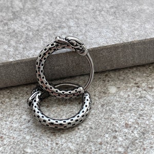 May include: A pair of silver hoop earrings with a textured design. The top of one earring features a snake head.