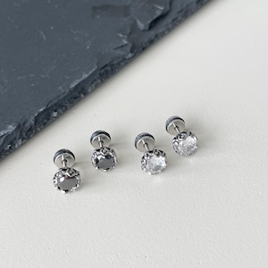 May include: Four silver stud earrings with clear and black gemstones. The earrings have a decorative metal rim around the gemstones.