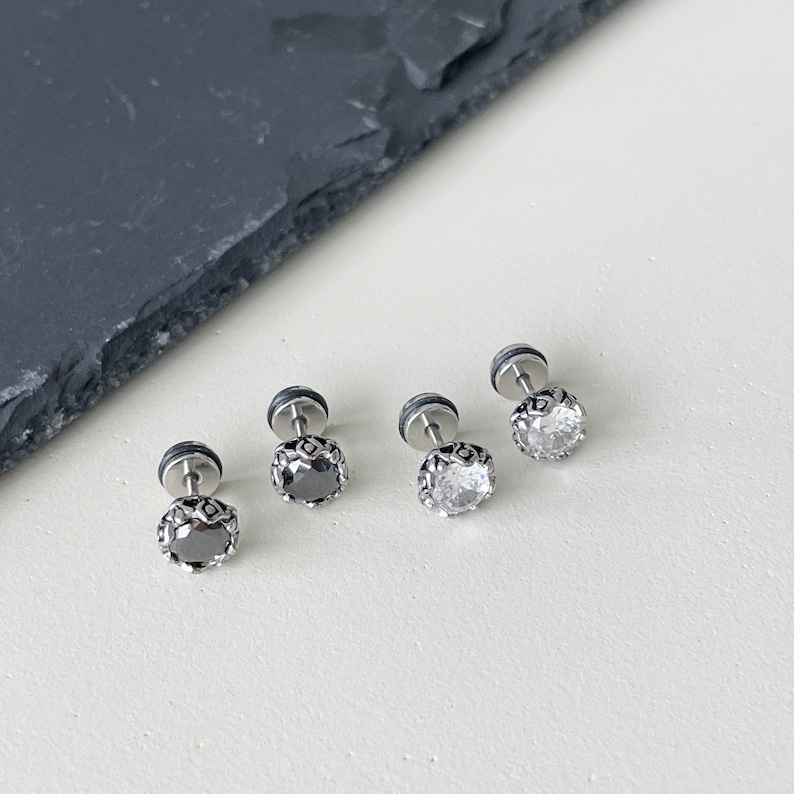 May include: Four silver stud earrings with clear and black gemstones. The earrings have a decorative metal rim around the gemstones.