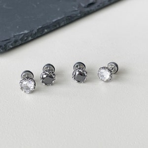 May include: Four silver earrings with a round, faceted stone in the center. Two earrings have a clear stone, and two earrings have a black stone.