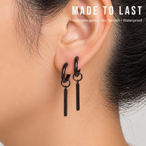 May include: Black hoop earrings with a rectangular bar pendant. The earrings are displayed on an ear. The image includes the text "MADE TO LAST" and the words "Hypoallergenic, No Tarnish, Waterproof".