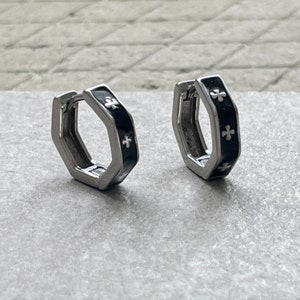Peut inclure: Une paire de boucles d'oreilles créoles hexagonales en argent avec émail noir et accents de croix blancs.