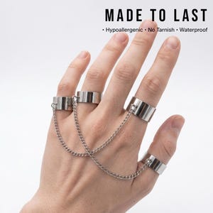 May include: Silver-toned rings connected by delicate chains. The rings are wide bands, and the chains link them together. The image includes the text "MADE TO LAST" with additional text below indicating the rings are hypoallergenic, no tarnish, and waterproof.