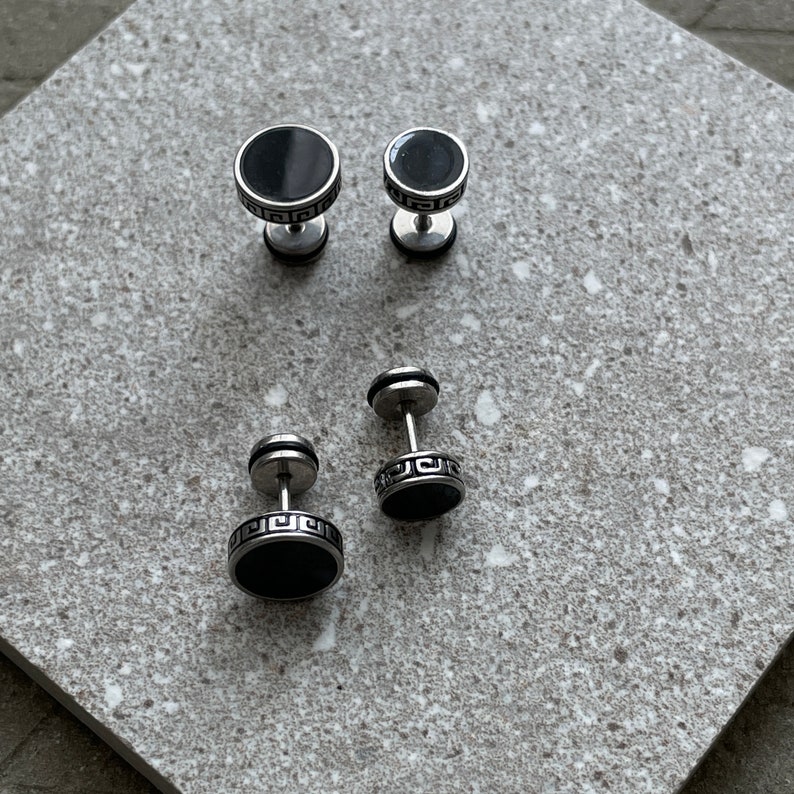 K&ouml;nnte beinhalten: Vier Paar Edelstahl-Ohrstecker mit schwarzen, kreisf&ouml;rmigen Mittelst&uuml;cken. Zwei Paare haben eine kleinere Gr&ouml;&szlig;e, die anderen beiden Paare eine gr&ouml;&szlig;ere Gr&ouml;&szlig;e. Die Ohrringe haben ein griechisches Schl&uuml;sseldesign um den schwarzen Mittelpunkt.