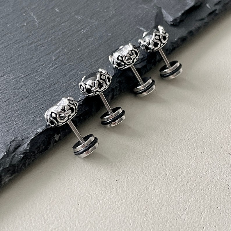 May include: Four silver and black ear studs with a crown design. The studs have a small clear stone in the center of the crown.