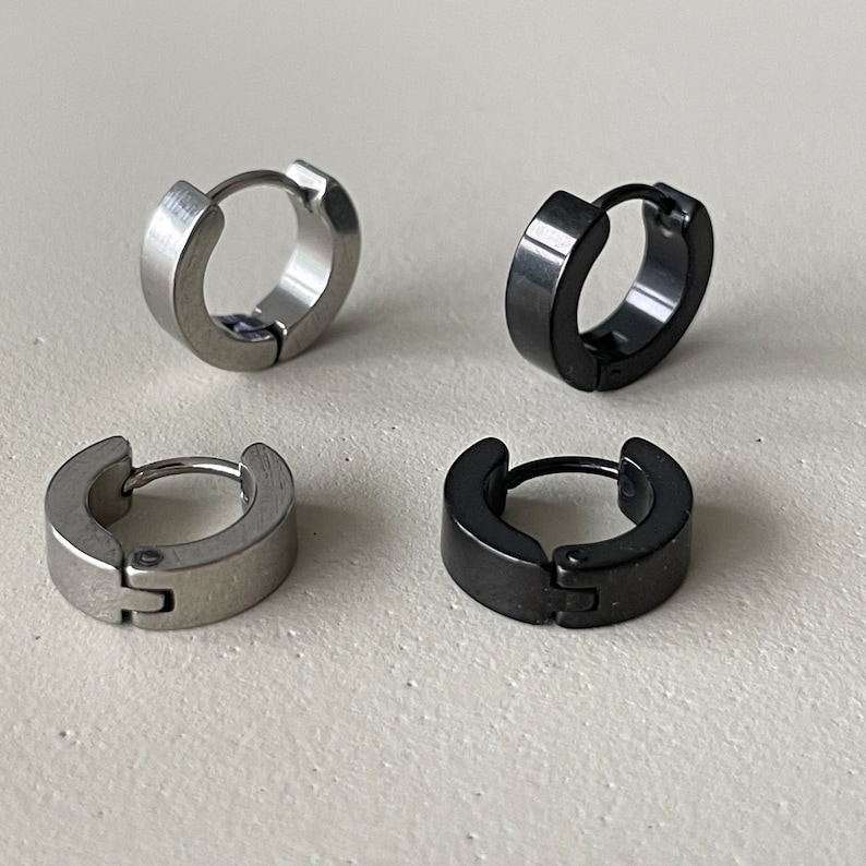Pu&ograve; includere: Quattro piccoli orecchini a cerchio. Due sono color argento e due sono neri. Gli orecchini hanno un design a cerniera per una facile indossabilit&agrave;. Gli orecchini sono su una superficie di colore chiaro.