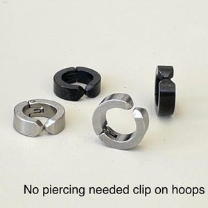 Pu&ograve; includere: Sono mostrati quattro orecchini a cerchio a clip. Due sono color argento e due sono neri. Il testo in basso nell'immagine recita "No piercing needed clip on hoops."