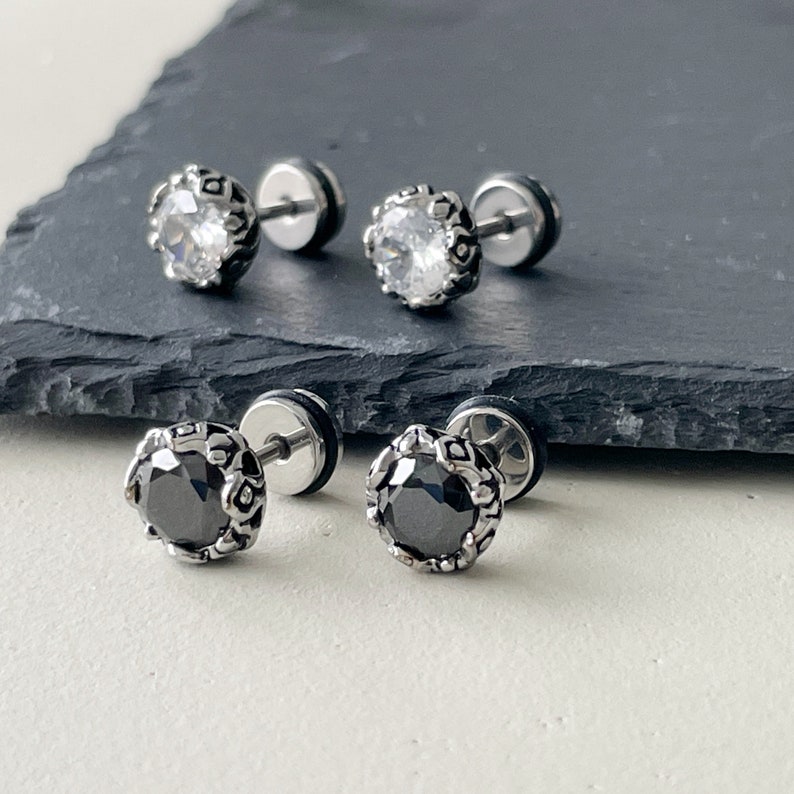 May include: A pair of silver earrings with black and white round stones set in a decorative frame. The earrings have a push-back closure.