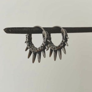 May include: A pair of silver hoop earrings with a textured finish and sharp spikes around the edge.